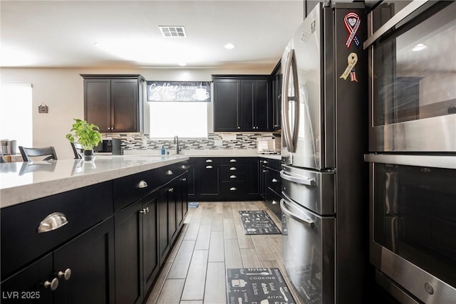 kitchen featuring visible vents, tasteful backsplash, a sink, light stone counters, and stainless steel appliances