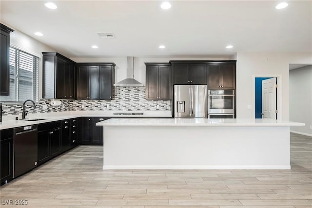 10126 Cliff Dwellings Ave, Las Vegas, NV 89178 - kitchen with stainless steel appliances, wall chimney range hood, backsplash, a kitchen island, and light wood-style floors