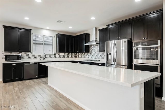 10126 Cliff Dwellings Ave, Las Vegas, NV 89178 - kitchen with stainless steel appliances, wall chimney exhaust hood, dark cabinetry, light wood finished floors, and tasteful backsplash
