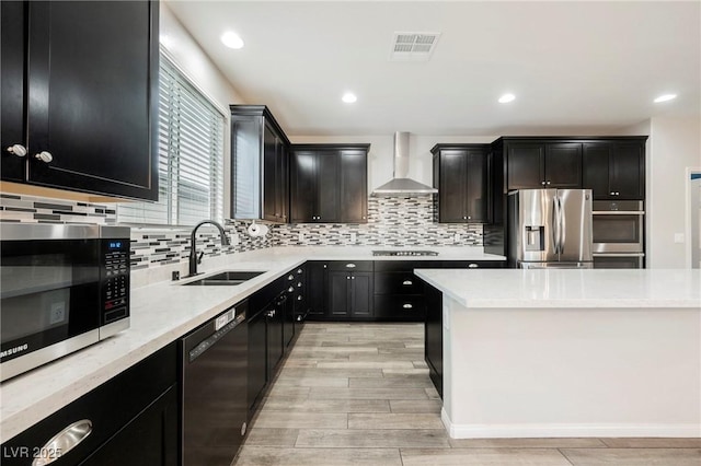 10126 Cliff Dwellings Ave, Las Vegas, NV 89178 - kitchen featuring stainless steel appliances, wall chimney exhaust hood, light wood-style floors, backsplash, and dark cabinetry