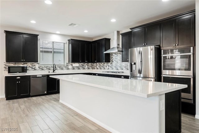 10126 Cliff Dwellings Ave, Las Vegas, NV 89178 - kitchen featuring stainless steel appliances, wall chimney range hood, dark cabinets, a center island, and recessed lighting