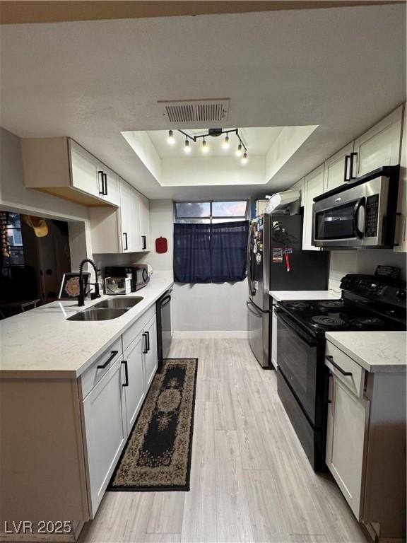kitchen featuring a raised ceiling, visible vents, a sink, black appliances, and light wood-style flooring