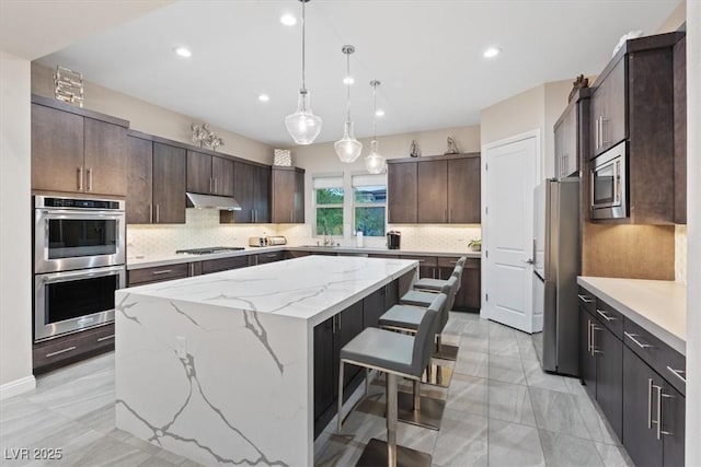 10018 Regency Square Ave, Las Vegas, NV 89148 - kitchen featuring stainless steel appliances, under cabinet range hood, a center island, dark brown cabinetry, and decorative backsplash
