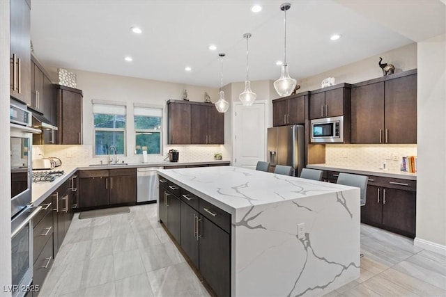 10018 Regency Square Ave, Las Vegas, NV 89148 - kitchen featuring stainless steel appliances, a kitchen island, decorative backsplash, dark brown cabinetry, and hanging light fixtures