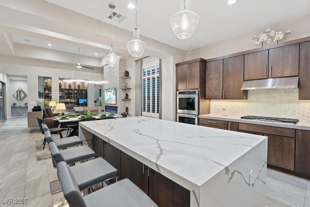 10018 Regency Square Ave, Las Vegas, NV 89148 - kitchen with under cabinet range hood, stainless steel double oven, tasteful backsplash, gas cooktop, and open floor plan