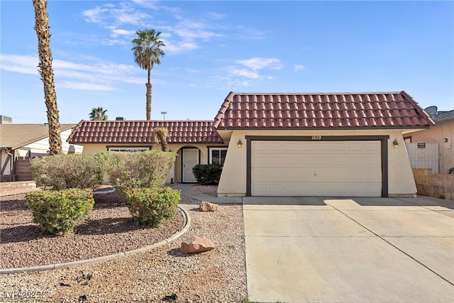 mediterranean / spanish house with an attached garage, a tiled roof, stucco siding, and concrete driveway