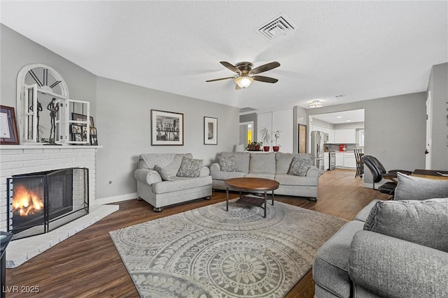 living room with wood finished floors, a ceiling fan, visible vents, and a brick fireplace