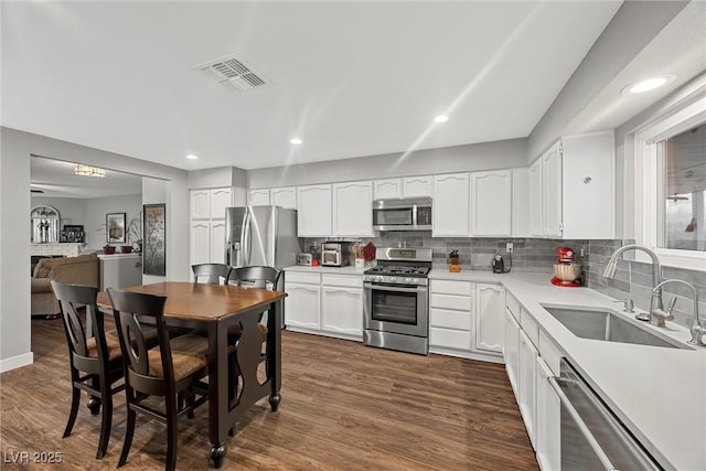 kitchen featuring a sink, backsplash, appliances with stainless steel finishes, dark wood-type flooring, and visible vents