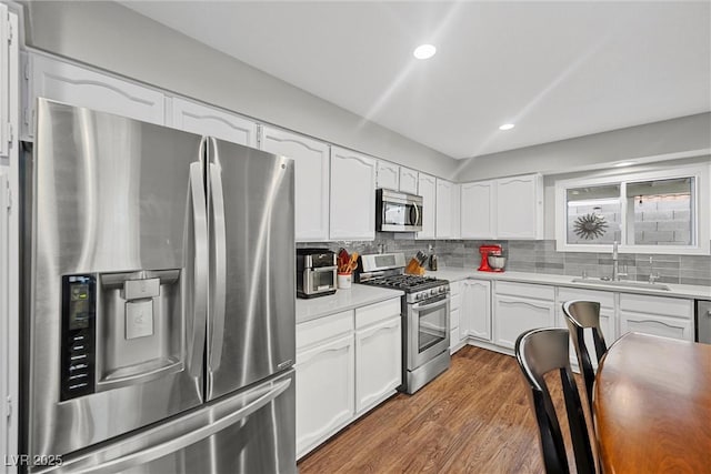 kitchen with a sink, white cabinetry, decorative backsplash, wood finished floors, and appliances with stainless steel finishes