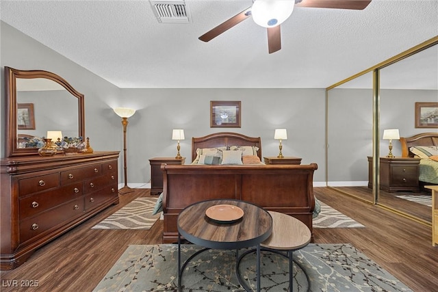 bedroom with dark wood-style floors, baseboards, a textured ceiling, and visible vents