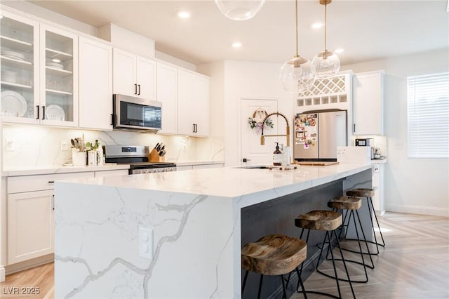 kitchen featuring glass insert cabinets, appliances with stainless steel finishes, an island with sink, and white cabinetry