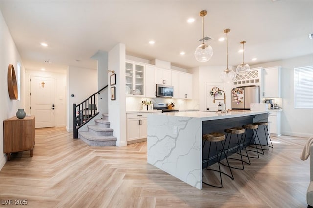 kitchen with white cabinets, a center island with sink, baseboards, glass insert cabinets, and appliances with stainless steel finishes