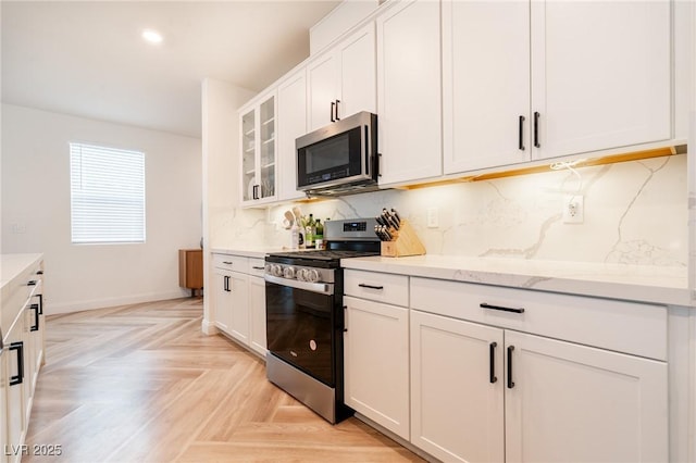 kitchen with stainless steel appliances, light stone countertops, decorative backsplash, glass insert cabinets, and white cabinetry
