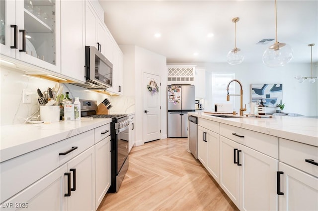kitchen with white cabinets, visible vents, a sink, glass insert cabinets, and appliances with stainless steel finishes