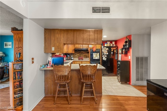 kitchen with brown cabinets, a peninsula, black appliances, and visible vents