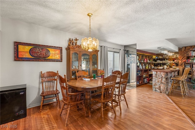 dining area featuring an inviting chandelier, a dry bar, wood finished floors, and a textured ceiling
