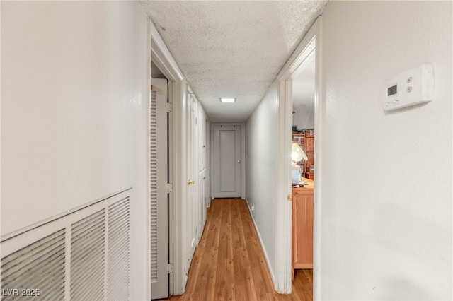corridor with light wood-style floors, a textured ceiling, and baseboards