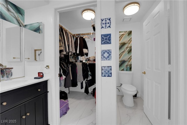 bathroom featuring toilet, marble finish floor, vanity, and a spacious closet