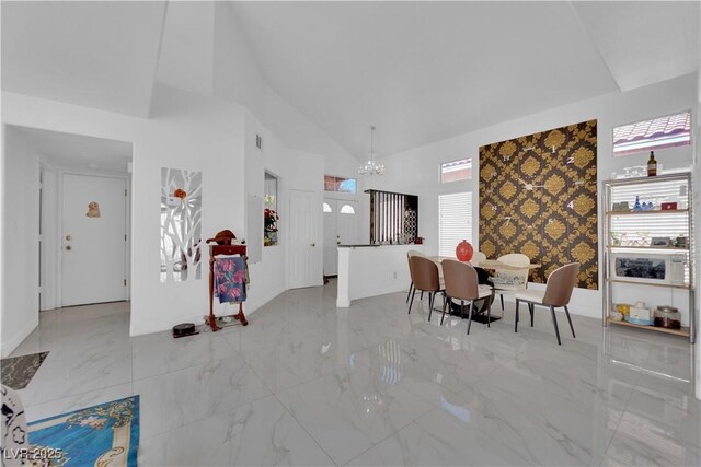 dining room featuring a notable chandelier, high vaulted ceiling, marble finish floor, an accent wall, and wallpapered walls