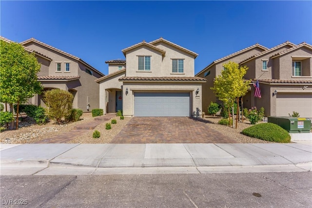 mediterranean / spanish-style home featuring an attached garage, a tiled roof, stucco siding, and decorative driveway
