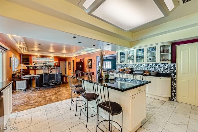 7165 Mira Monte Cir, Las Vegas, NV 89120 - kitchen featuring a tray ceiling, dark countertops, glass insert cabinets, marble finish floor, and a breakfast bar