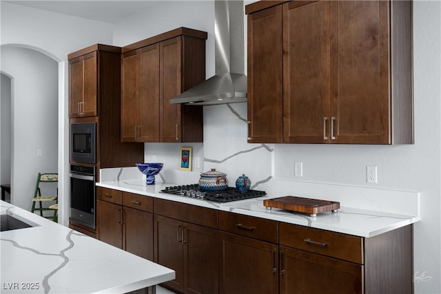 1130 Calico Rdg, Mesquite, NV 89034 - kitchen with appliances with stainless steel finishes, wall chimney range hood, arched walkways, light stone countertops, and dark brown cabinetry