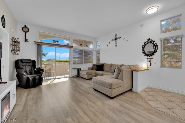 living room featuring a glass covered fireplace, baseboards, and light wood-style floors