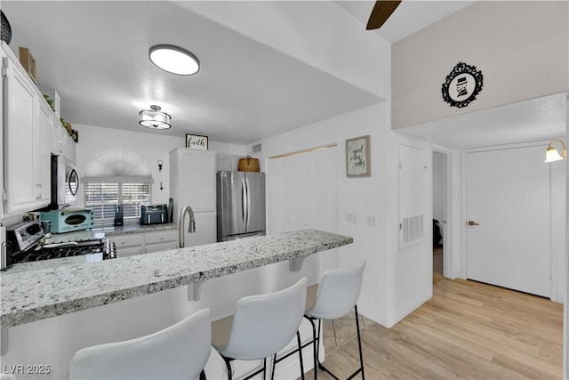 kitchen featuring a breakfast bar, a sink, white cabinets, and appliances with stainless steel finishes