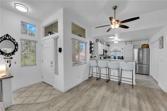 kitchen with a breakfast bar, stainless steel appliances, ceiling fan, light wood-type flooring, and a peninsula
