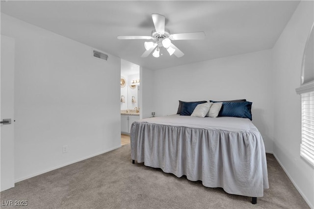 bedroom featuring ensuite bath, light colored carpet, ceiling fan, baseboards, and visible vents