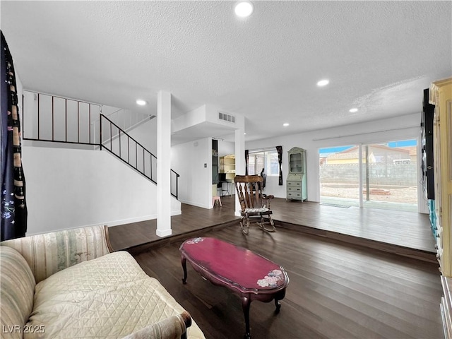 living area with visible vents, wood finished floors, a textured ceiling, and stairs