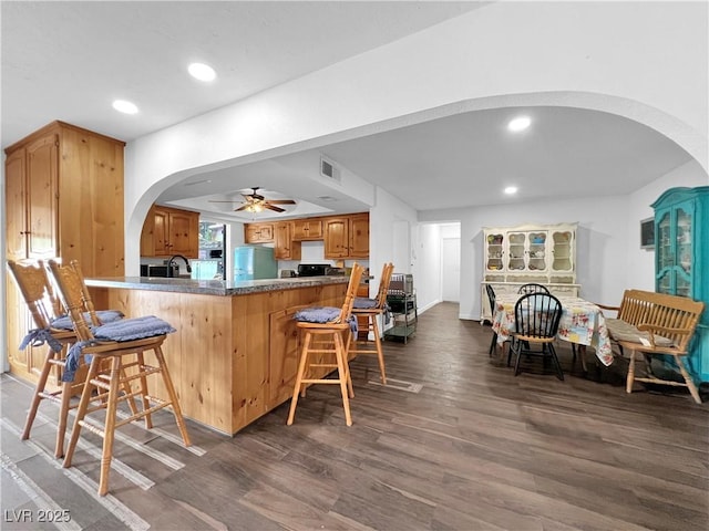 kitchen featuring refrigerator, a ceiling fan, a kitchen breakfast bar, arched walkways, and dark wood-style floors