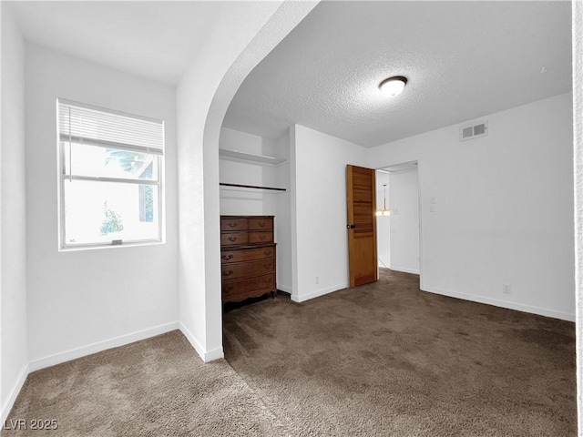 unfurnished bedroom with dark colored carpet, visible vents, arched walkways, baseboards, and a textured ceiling