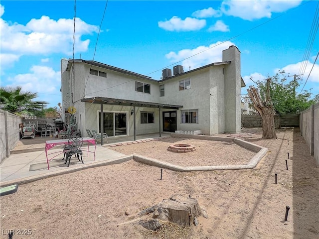 rear view of property with stucco siding, a patio area, a fenced backyard, and an outdoor fire pit
