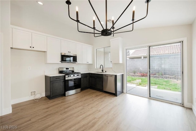 kitchen with an inviting chandelier, light wood-style floors, light countertops, white cabinets, and appliances with stainless steel finishes