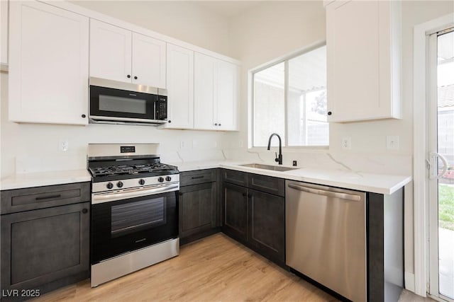 kitchen with white cabinets, light stone countertops, a sink, light wood-style floors, and stainless steel appliances
