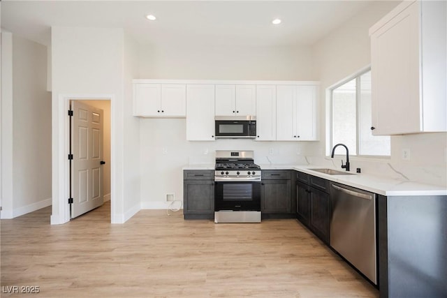 kitchen featuring appliances with stainless steel finishes, a sink, baseboards, light wood finished floors, and white cabinetry