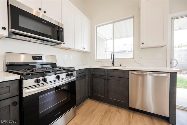 kitchen with a sink, appliances with stainless steel finishes, white cabinets, and light wood-type flooring