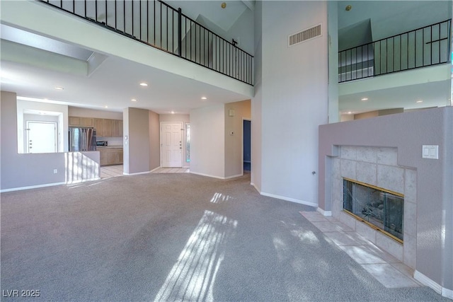unfurnished living room with light colored carpet, a high ceiling, a tile fireplace, and visible vents