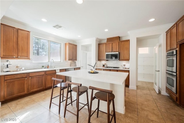 kitchen featuring stainless steel appliances, backsplash, visible vents, a sink, and a kitchen bar