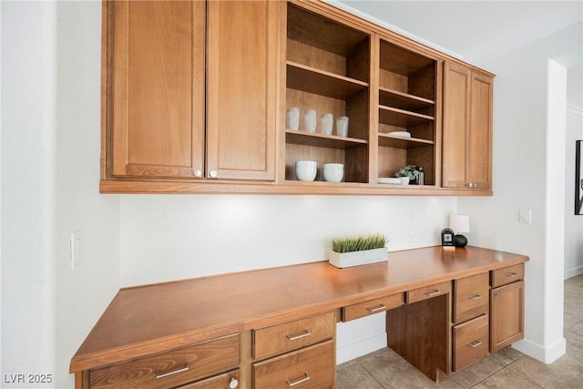 unfurnished office with baseboards, light tile patterned flooring, and built in desk
