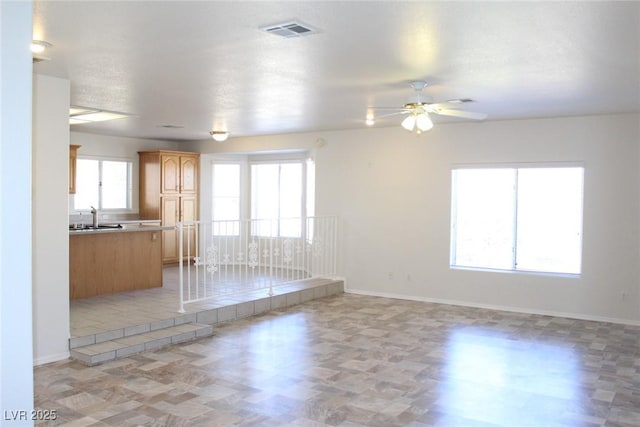 unfurnished living room featuring baseboards, a ceiling fan, visible vents, and a sink
