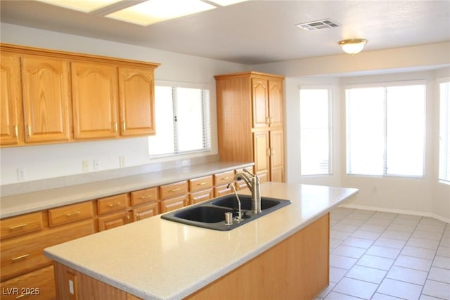 kitchen featuring light countertops, visible vents, light tile patterned floors, a sink, and a center island with sink