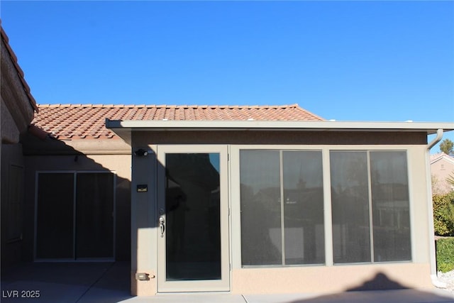 back of house featuring a tile roof and stucco siding