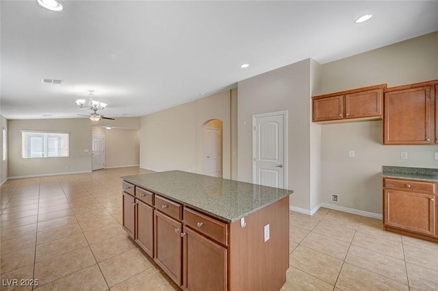 7822 Whitlocks Mill Ave, Las Vegas, NV 89147 - kitchen with light tile patterned floors, brown cabinets, arched walkways, a center island, and baseboards