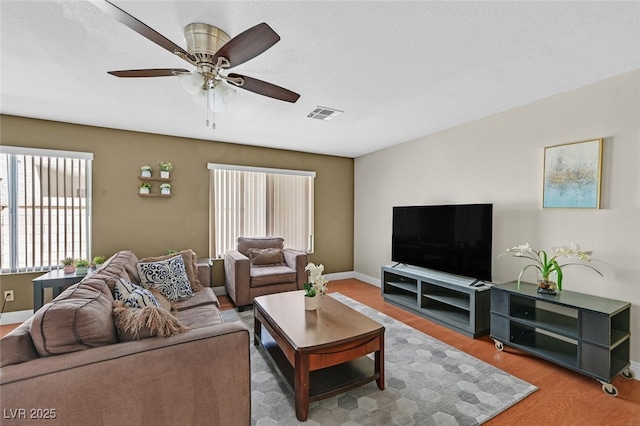 living room with baseboards, wood finished floors, visible vents, and ceiling fan