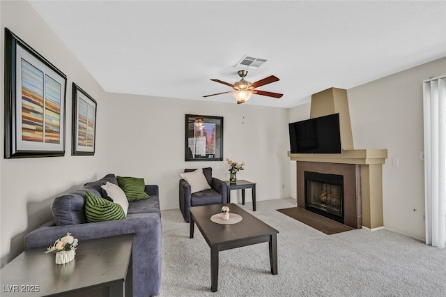 carpeted living area with a tile fireplace, visible vents, and ceiling fan