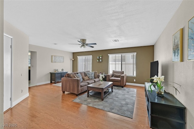 living room with baseboards, light wood-style flooring, visible vents, and a ceiling fan