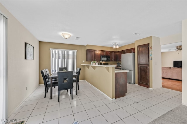 kitchen featuring a peninsula, light countertops, freestanding refrigerator, black microwave, and a breakfast bar