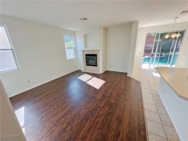 unfurnished living room featuring light wood finished floors, baseboards, a tiled fireplace, and visible vents
